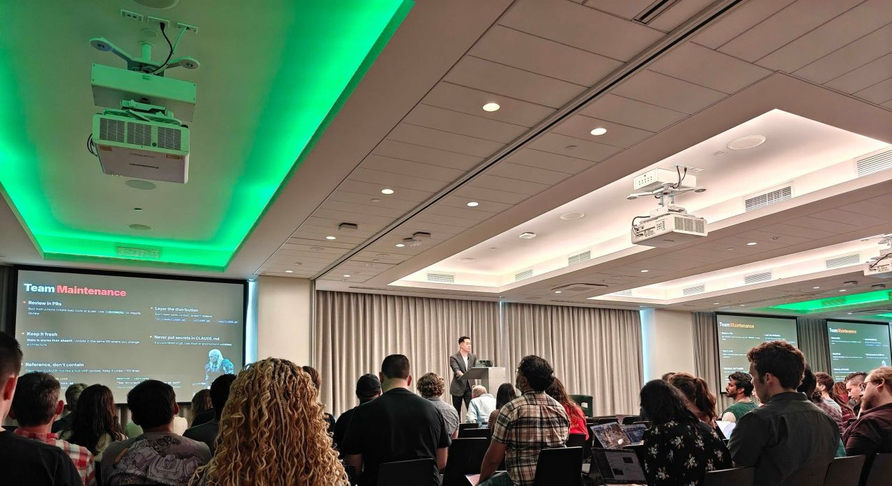 Alex Tong presenting to a large seated audience, with his slides displayed across the room.